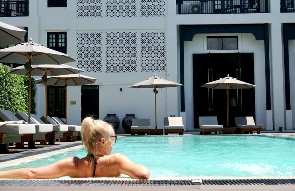 Woman relaxing in the saltwater pool by Burisiri's white Lanna lattice wall and grey umbrellas
