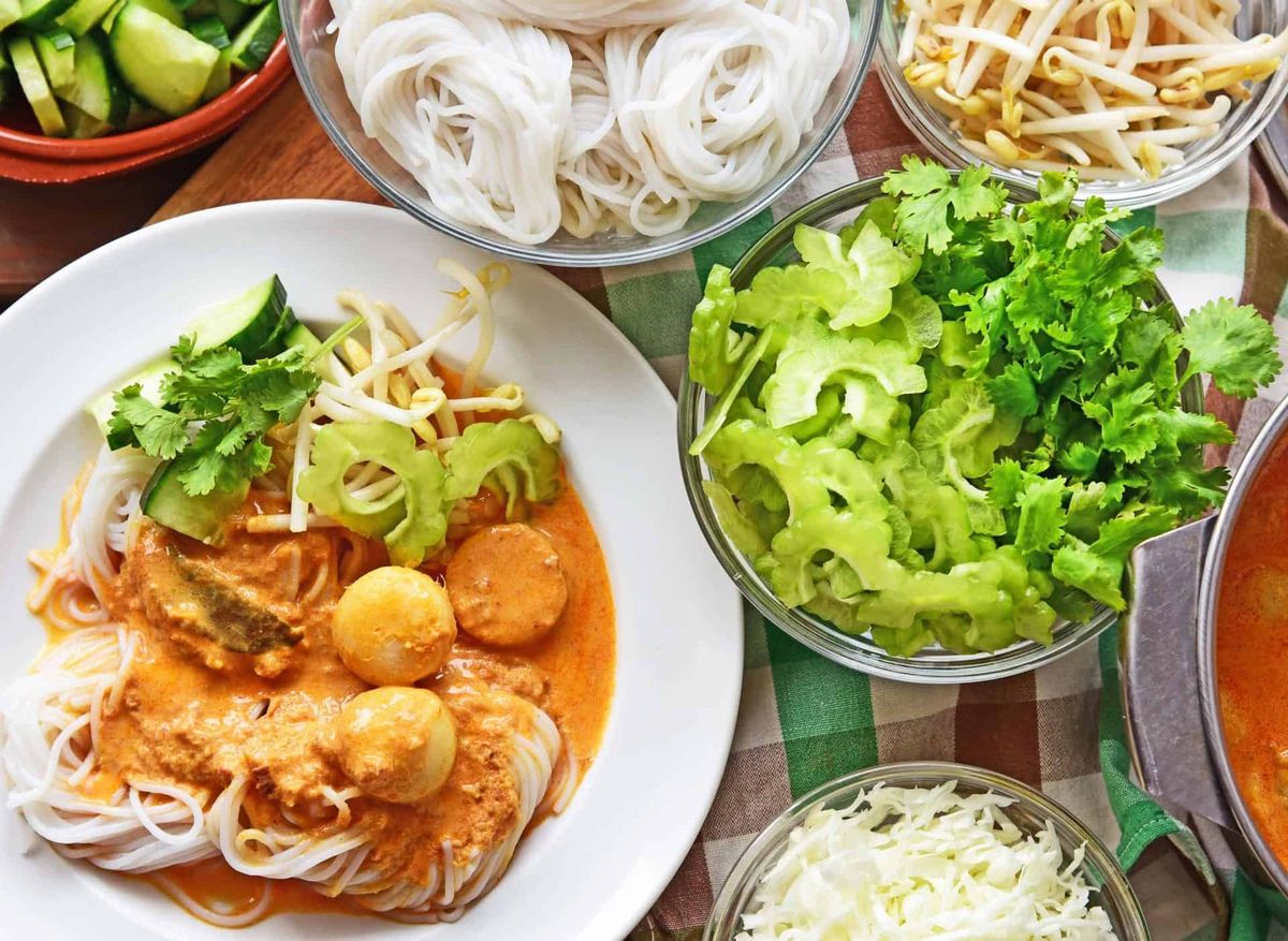 Plate of khanom jeen rice noodles with nam ngiao curry, bitter melon, bean sprouts and fresh herbs