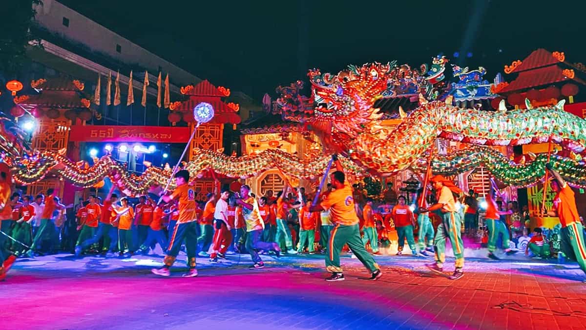 Nighttime dragon dance with orange-clad performers carrying a glowing illuminated dragon during Chinese New Year in Chiang Mai