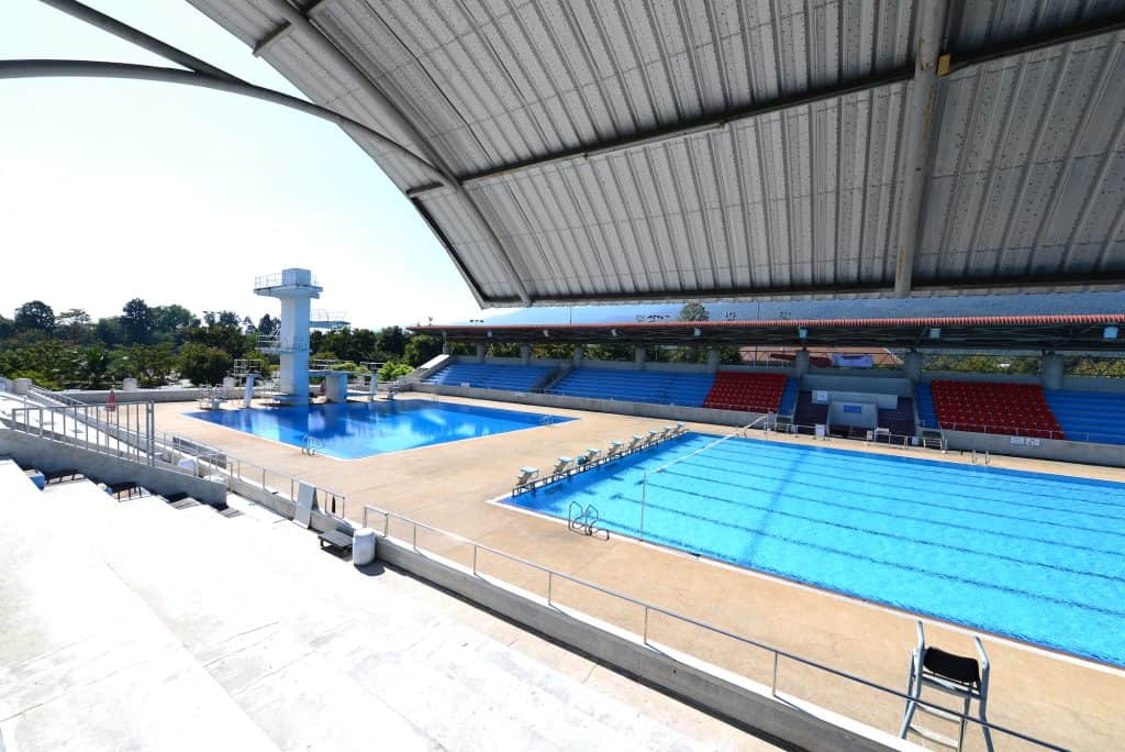 Covered Olympic pool and diving pool with tower and blue-and-red grandstands at 700 Years Stadium