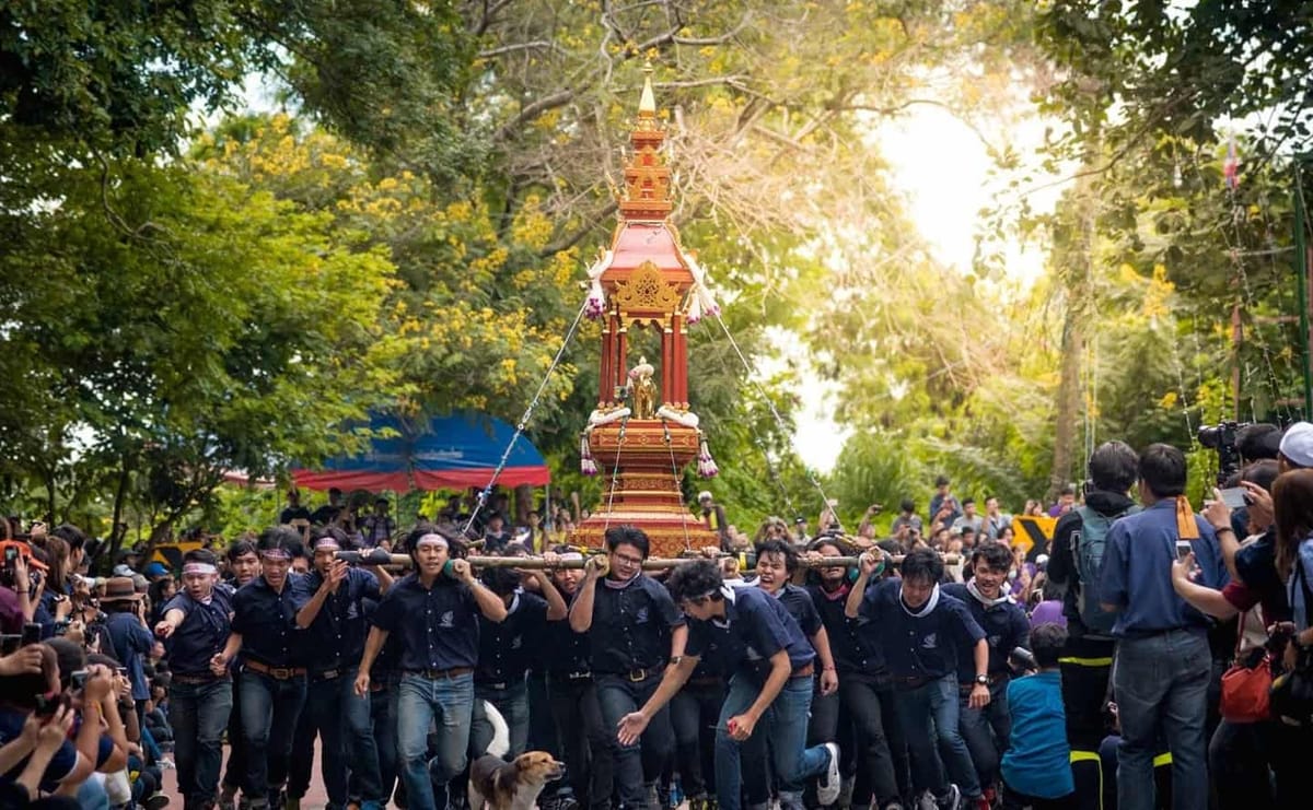 Crowds in dark blue shirts carrying an ornate gold-and-red reliquary on poles during the Doi Suthep Pilgrimage