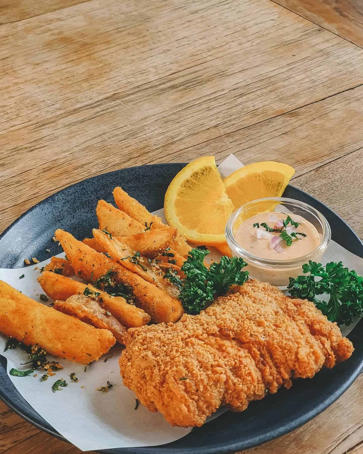 Plate of crumbed fried fish with potato wedges, parsley garnish, citrus wedges and a tartare-style dip at The Barn Eatery & Design