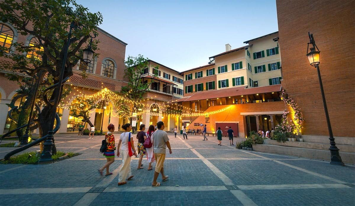 People strolling the Italianate brick piazza of One Nimman at dusk, lit by hanging string lights