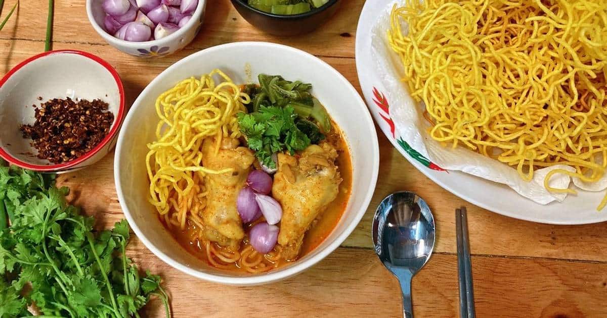 Bowl of northern khao soi, egg noodles in coconut curry with chicken, crispy noodles, shallots and lime