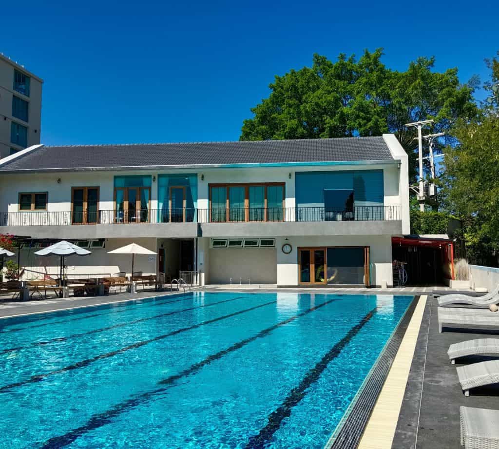 25m lap pool with lane lines and loungers below Looper's two-story building in Jed Yod