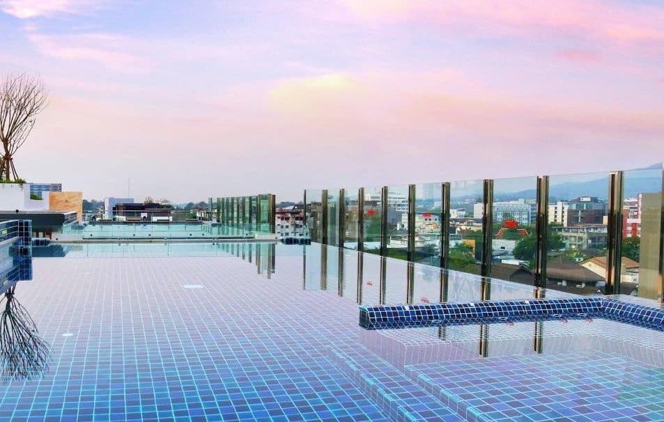 Blue-tiled rooftop infinity pool at Stay with Nimman under a pastel dusk sky over the city