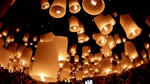 Thousands of glowing paper lanterns rising into the night sky at Yi Peng festival