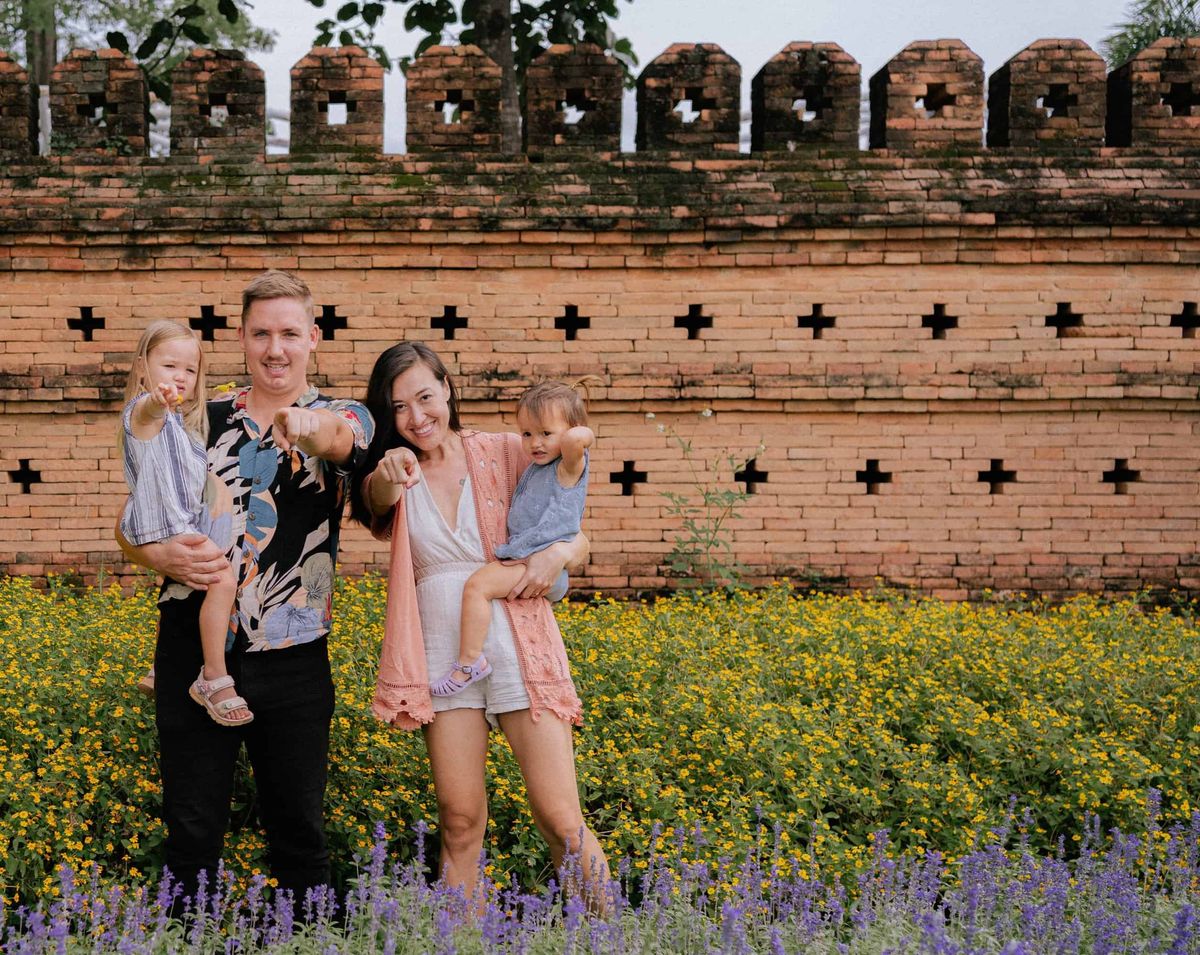 A family of four pointing at the camera in a wildflower field by Chiang Mai's old brick city wall