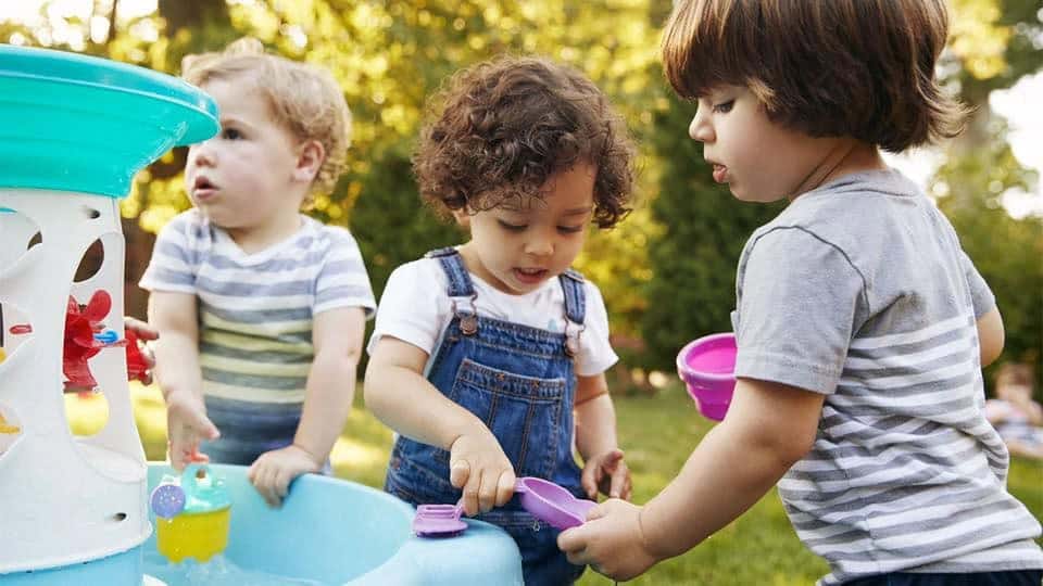 Three toddlers playing together at an outdoor water table, like a Little Owls Playgroup meetup in Chiang Mai