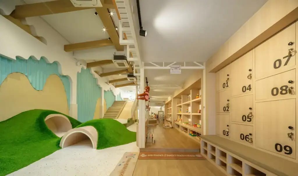 Wooden Ville Kids Cafe play area with grassy turf mounds, crawl tunnels, toy shelves and numbered lockers