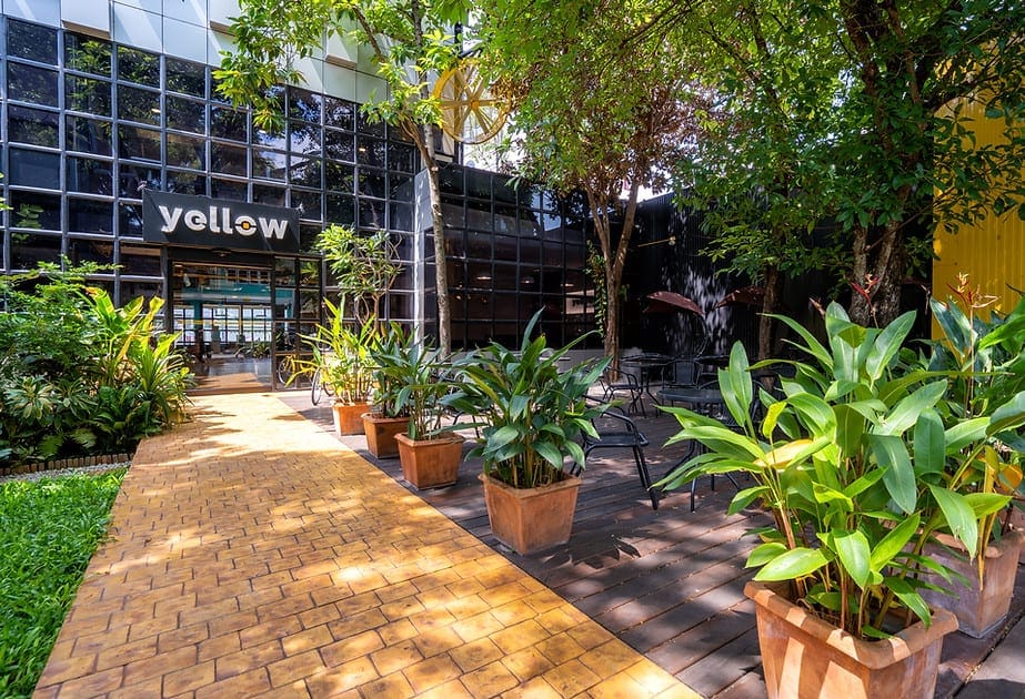 Entrance to Yellow Coworking in Nimmanhaemin, with a brick pathway lined by potted plants and outdoor seating
