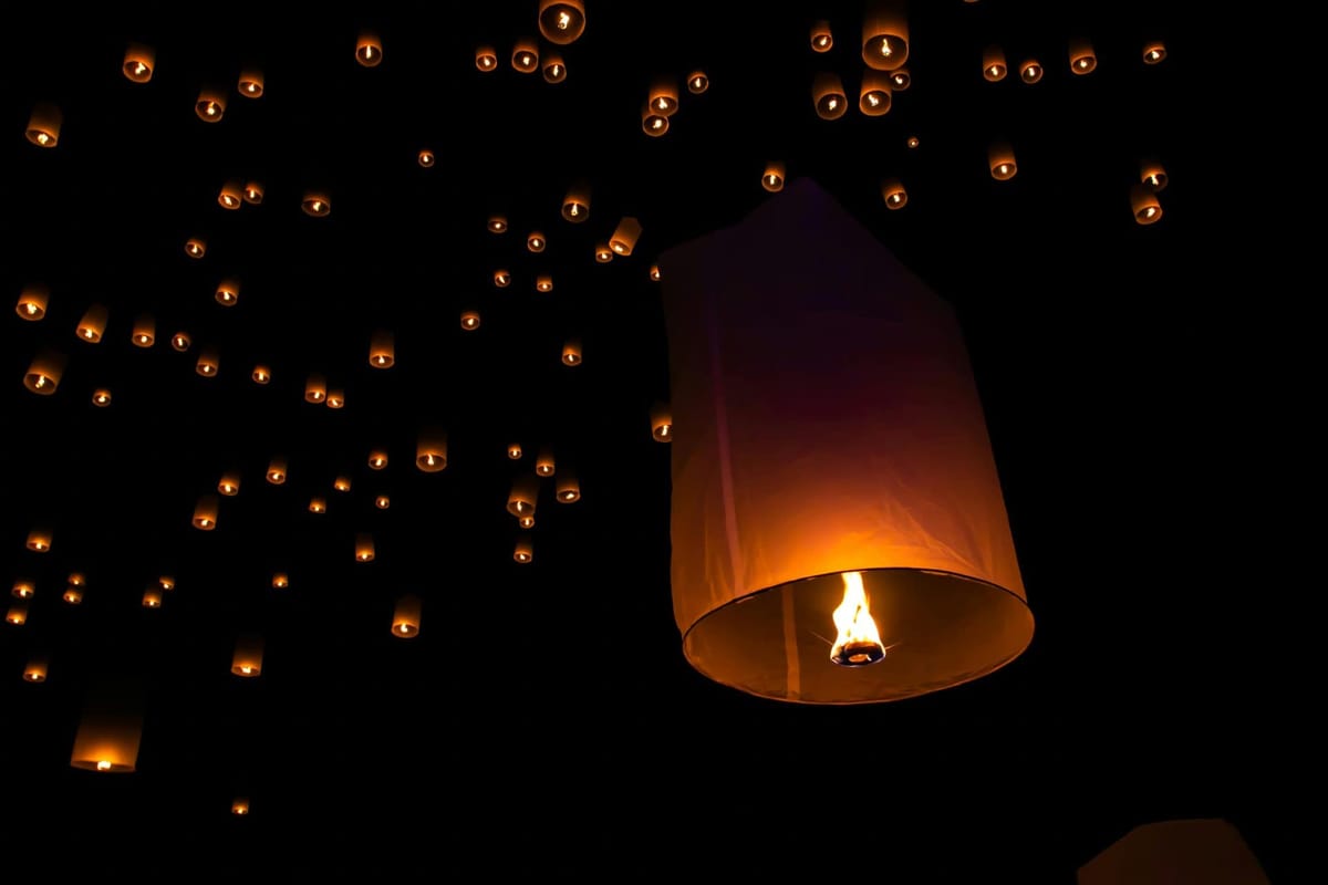 Glowing paper sky lanterns floating into the night sky during Yi Peng, Chiang Mai's Festival of Lights