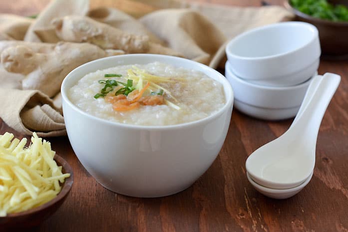 Bowl of Thai rice porridge (jok) topped with shredded ginger and spring onion, with ginger root and spoons