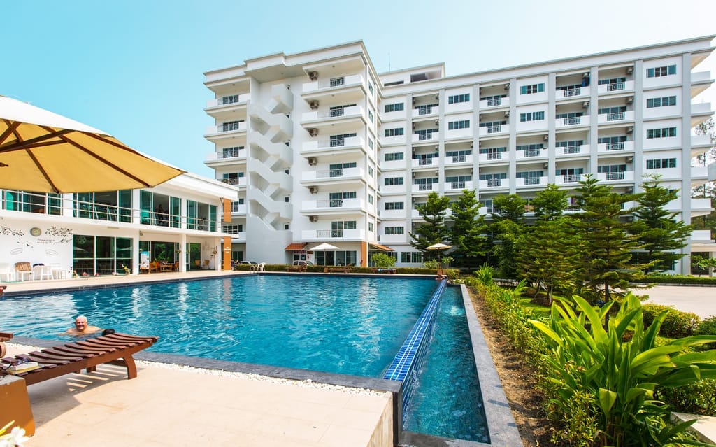 Saltwater pool and loungers beside the tall white Greenhill Condo tower, a man resting under a yellow umbrella