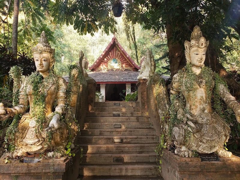 Stone staircase to Wat Pha Lat's ornate Lanna temple in the forest, flanked by two mossy guardian deity statues