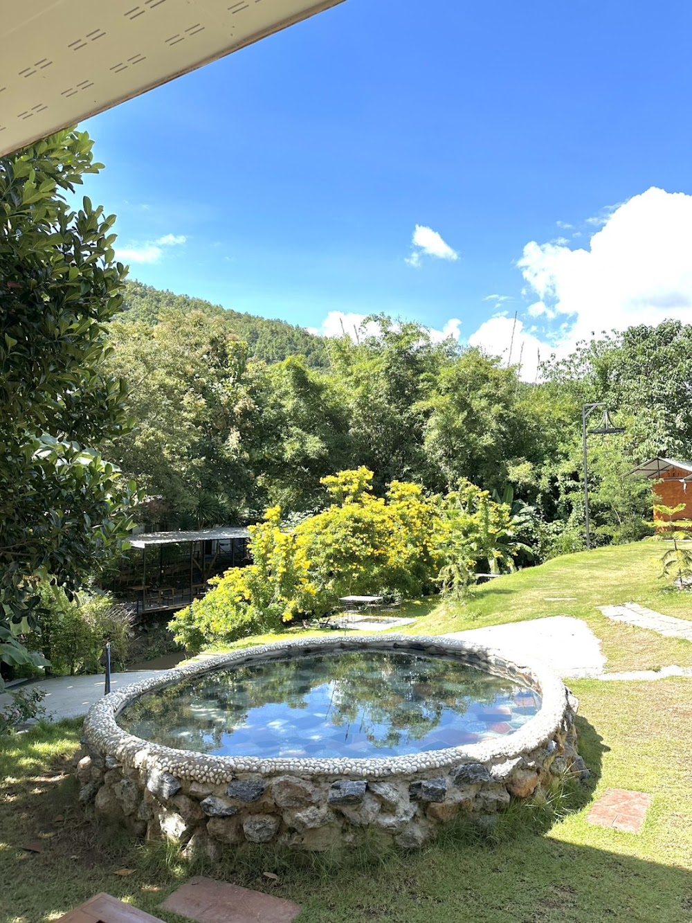 A round stone-rimmed cold plunge pool reflecting the sky in Eudemonia's garden below green hills