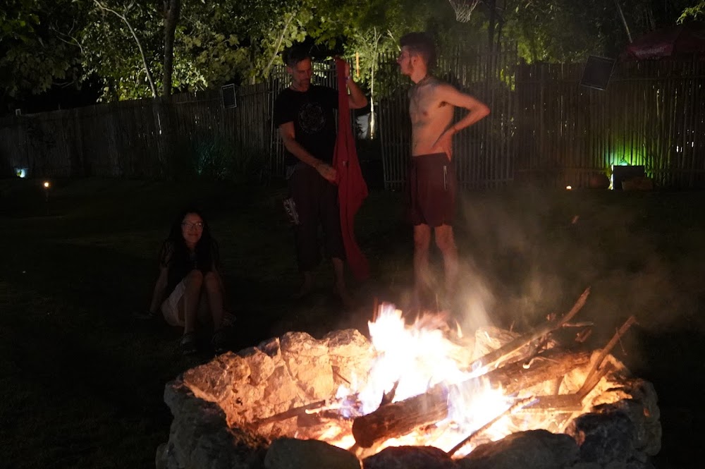 People gathered around a roaring stone fire pit at night in Eudemonia's garden
