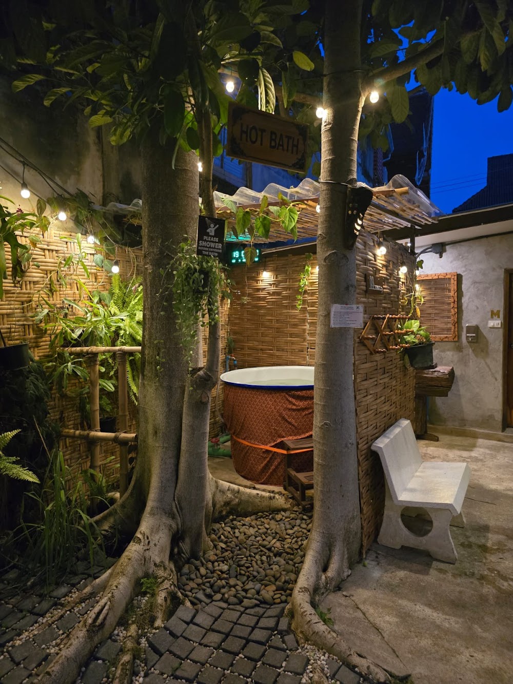 Evening spa garden at The Old City Spa with a wooden hot tub, festoon lights and a 'Hot Bath' sign