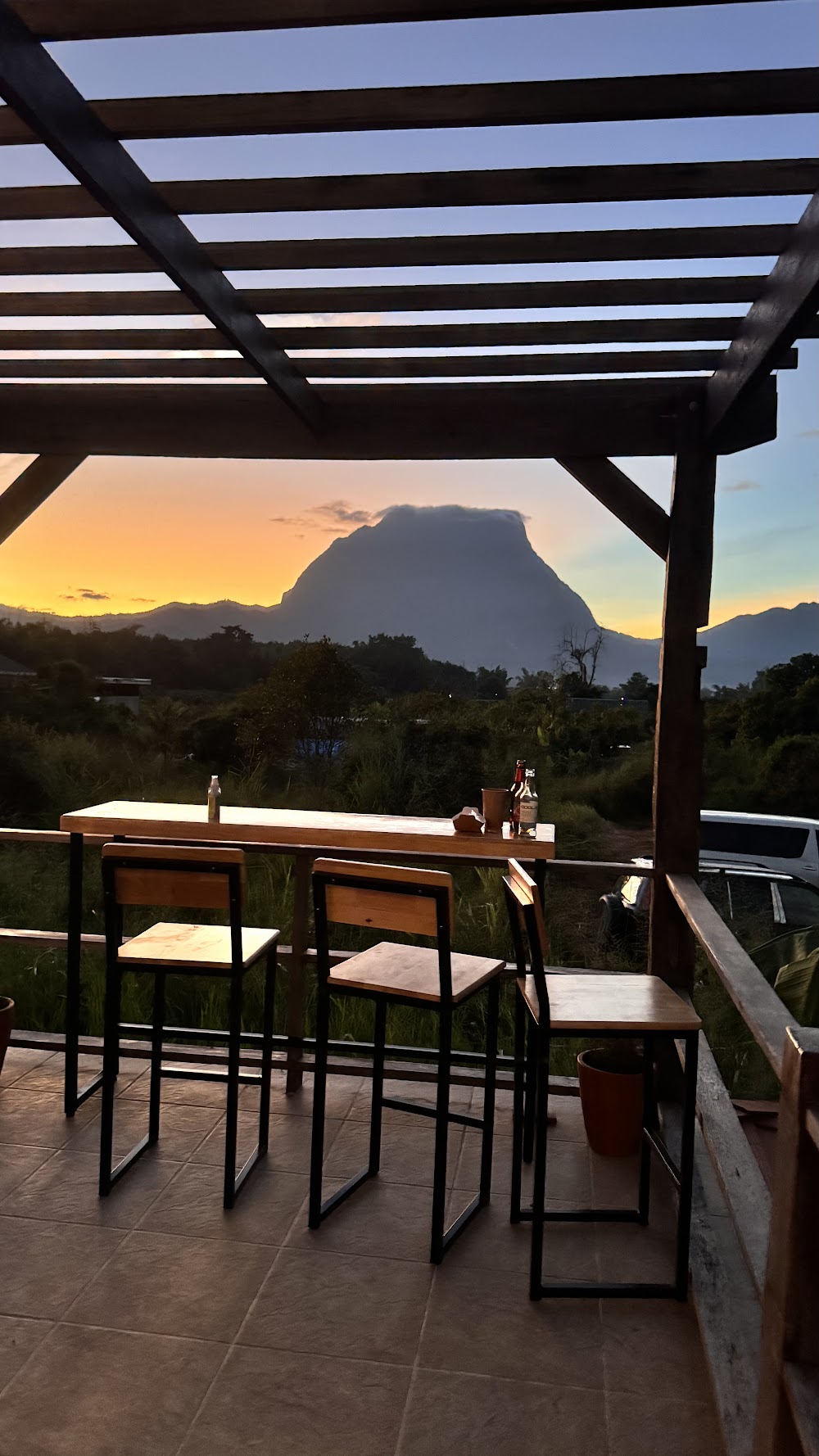 Covered terrace bar with wooden stools looking out to the Chiang Dao mountain silhouetted against an orange sunset