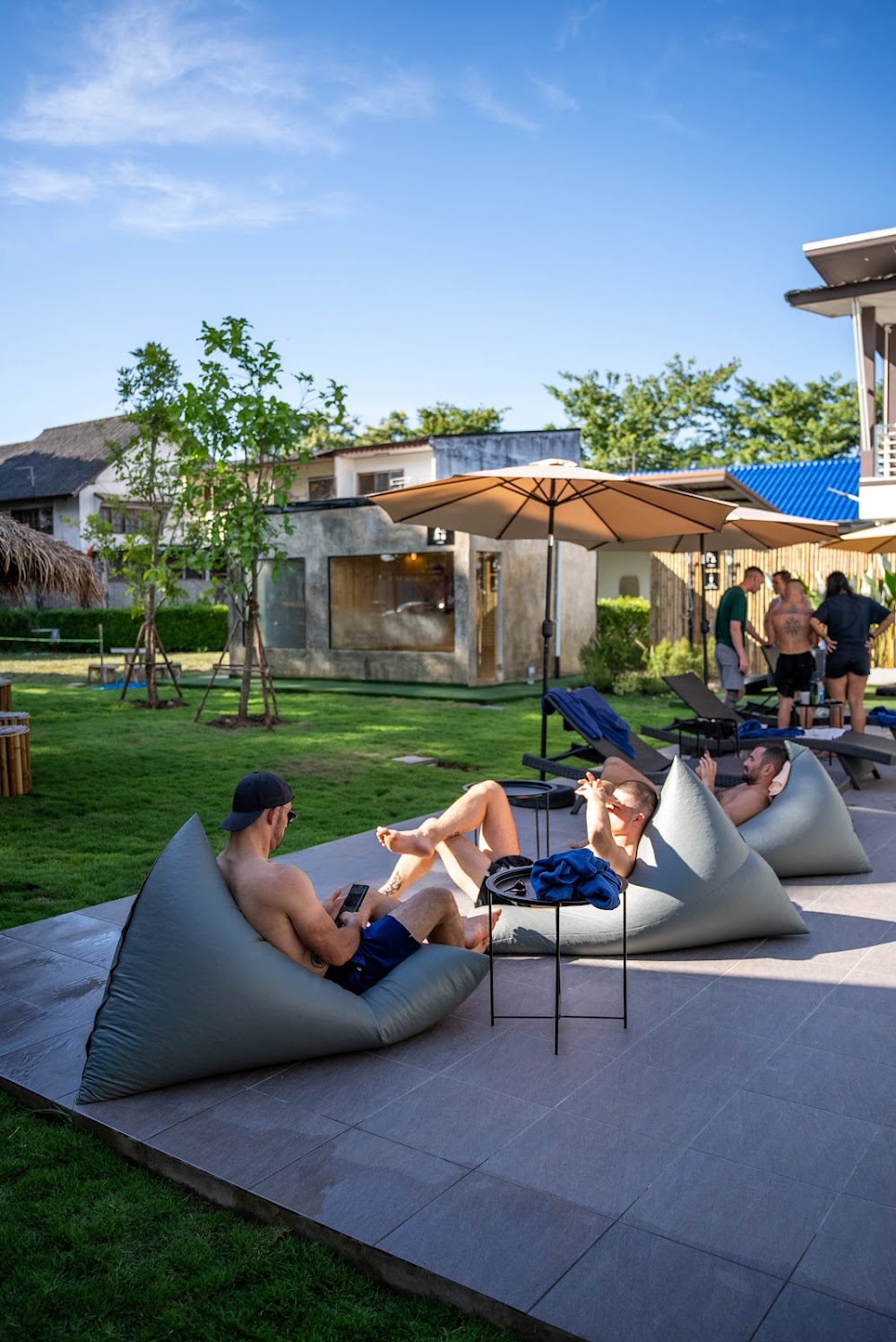 Guests relaxing on grey beanbag loungers by the pool near the steam cabin at Vibes Chiangmai