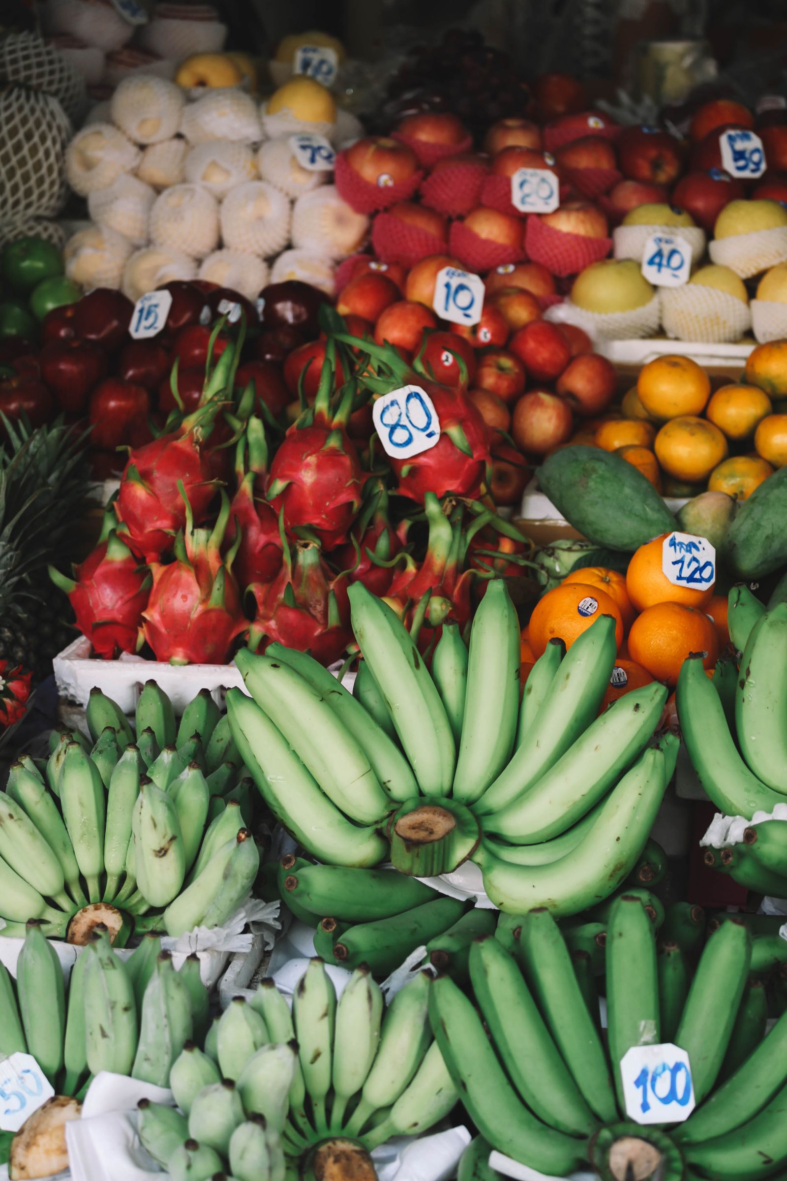 A Thai market fruit stall piled with dragonfruit, bananas, mangosteen and oranges with baht price tags