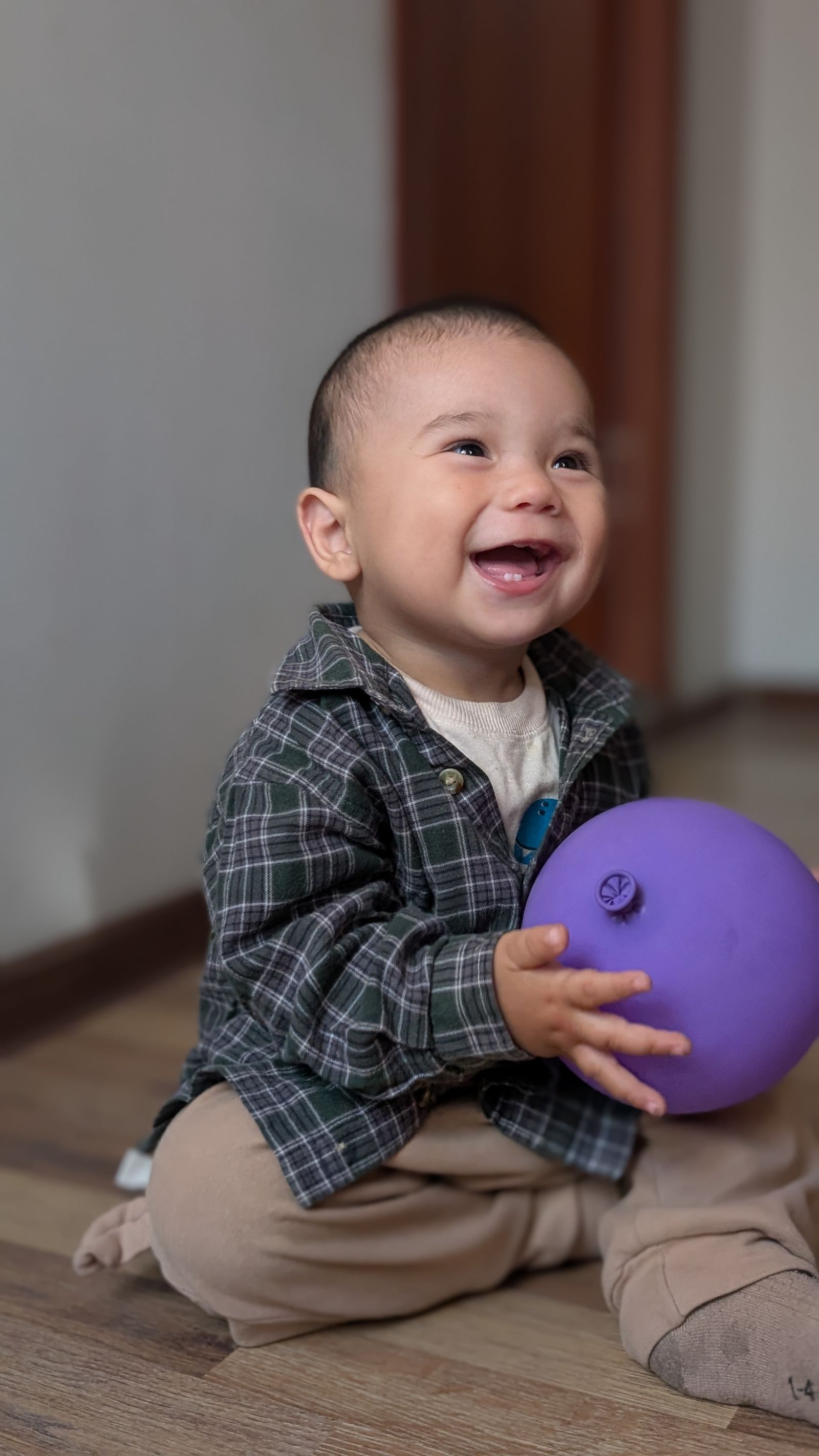 A laughing toddler sitting indoors holding a balloon