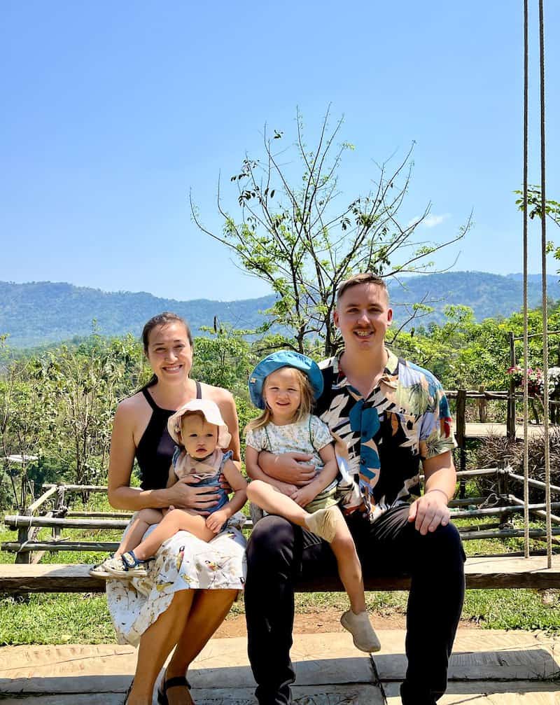 A family with two young children on a bench before Chiang Mai's green hills